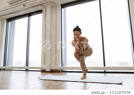 Lady balancing on one leg and keeping hands in namaste gesture at training room. Lady balancing on one leg and keeping hands in namaste gesture at training room. 111287076