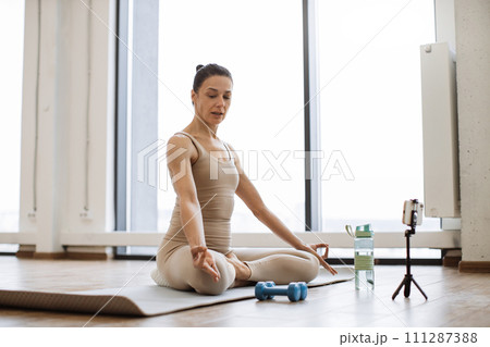 Professional female trainer recording video using tripod and smartphone. Professional female trainer recording video using tripod and smartphone. 111287388