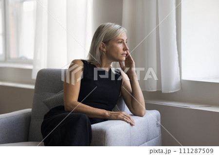 Attractive mature blonde woman relaxing alone seated on cozy armchair 111287509