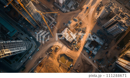 The aerial image captures the bustling activity of a construction site surrounded by buildings during the golden hour of dusk. The aerial image captures the bustling activity of a construction site surrounded by buildings during the golden hour of dusk. 111288671