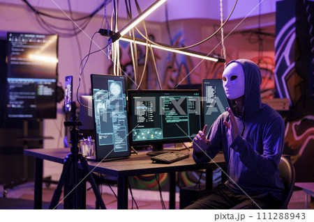 Hacker in anonymous mask recording video with online fraud on mobile phone while doing illegal activity. Internet scammer streaming threat to receive money and privacy information 111288943