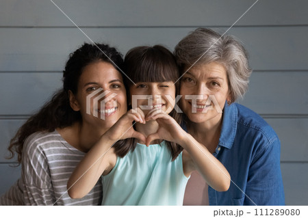 Loving grandma and mom cuddle little girl holding heart sign 111289080