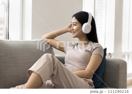 Positive relaxed young Asian music fan girl wearing wireless headphones 111290218
