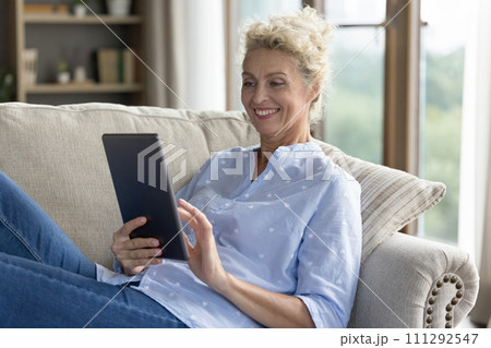 Smiling mature female resting on sofa with digital tablet Smiling mature female resting on sofa with digital tablet 111292547