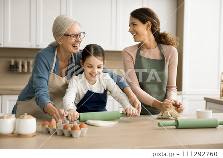 Cheerful grandma teaching granddaughter and adult daughter woman to bake Cheerful grandma teaching granddaughter and adult daughter woman to bake 111292760