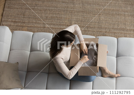 Woman sit on sofa opens courier parcel, top view Woman sit on sofa opens courier parcel, top view 111292795