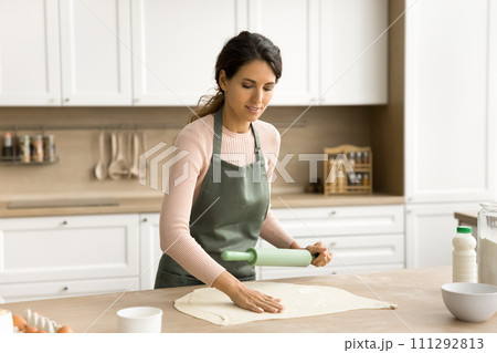 Positive pretty young Latin woman in apron baking in kitchen Positive pretty young Latin woman in apron baking in kitchen 111292813