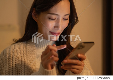 暗い部屋で深夜にスマホを見る若い女性 111295009