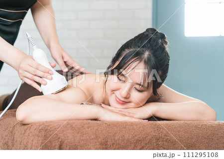 エステサロンでキャビテーション・エステマシンを使って痩身エステを行うエステティシャンと女性 111295108