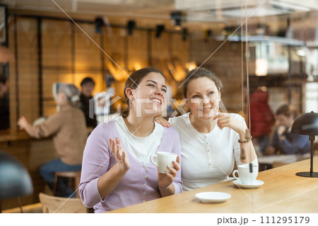 Carefree female colleagues drinking coffee and chatting in cafe Carefree female colleagues drinking coffee and chatting in cafe 111295179