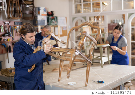 Portrait of middle-aged skillful repairman carpenter renovating chair furniture using tools in woodwork studio Portrait of middle-aged skillful repairman carpenter renovating chair furniture using tools in woodwork studio 111295473