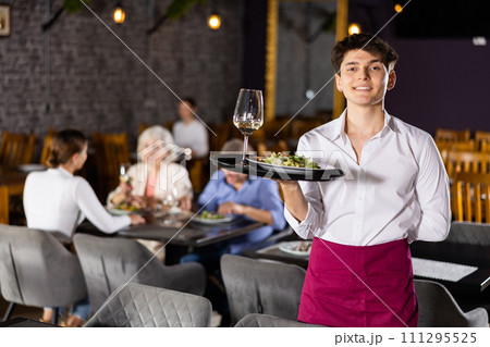 Young male waiter posing with tray in restaurant Young male waiter posing with tray in restaurant 111295525