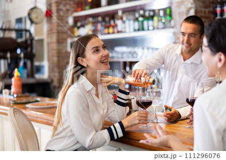 Two girlfriends chat with each other and drink red wine while sitting at bar in restaurant 111296076