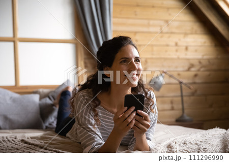 Dreamy young hispanic female lie on bed relax with smartphone Dreamy young hispanic female lie on bed relax with smartphone 111296990