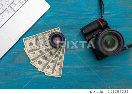 Earn money in internet DSLR camera, dollars, laptop, on blue wooden background, top view Earn money in internet DSLR camera, dollars, laptop, on blue wooden background, top view 111297281