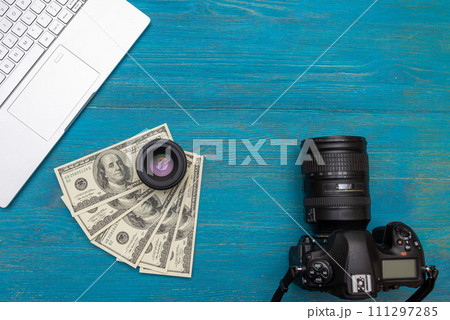 Earn money in internet DSLR camera, dollars, laptop, on blue wooden background, top view 111297285
