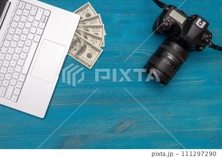 Earn money in internet DSLR camera, dollars, laptop, on blue wooden background, top view Earn money in internet DSLR camera, dollars, laptop, on blue wooden background, top view 111297290