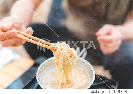 キャンプ飯でインスタントラーメン・袋麺を食べるキャンパーの男性 111297345