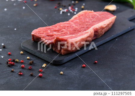 Raw fresh marbled meat and seasonings on dark background Raw fresh marbled meat and seasonings on dark background 111297505