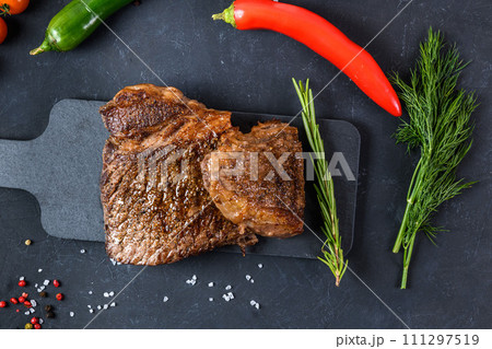 Grilled beef steak ribeye rare on on dark background top view Grilled beef steak ribeye rare on on dark background top view 111297519