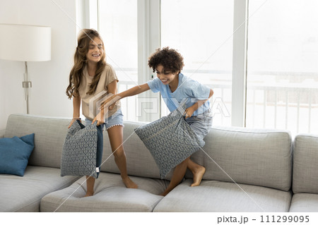 Happy excited preteen sibling kids fighting with pillows on couch Happy excited preteen sibling kids fighting with pillows on couch 111299095