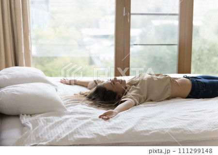 Young happy woman fell down on bed with arms raised 111299148