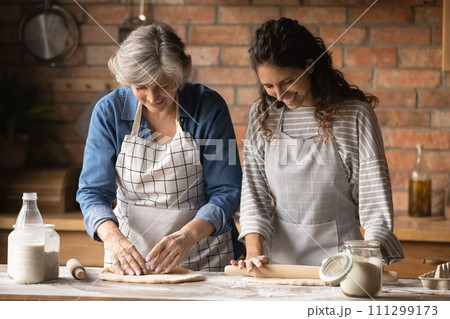 Older latin mother and daughter in law kneading rolling dough 111299173