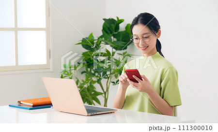 部屋でノートパソコンとスマホを使う女性 部屋でノートパソコンとスマホを使う女性 111300010