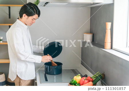 キッチンのHIコンロで煮込み料理をする若い男性 111301857