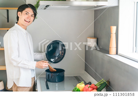 キッチンのHIコンロで煮込み料理をする若い男性 111301858