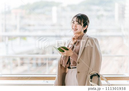 駅・公共施設で手帳を見て考えるビジネスウーマン（スケジュール・予定・アイデア・嬉しい） 111301938