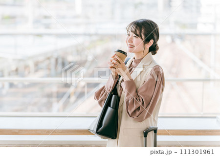 駅・ターミナルのエントランスでコーヒーを飲むビジネスウーマン（待ち合わせ・デート・待つ・温まる） 111301961