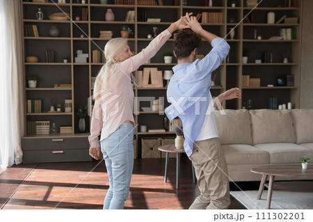 Older woman dance with young adult son at home 111302201