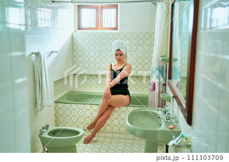 Woman in vintage bathroom enjoys leisurely bath, towel on head, leg outstretched. Female relaxes, self-care routine in retro designed home spa. Beauty ritual, alone time in old-fashioned setting. Woman in vintage bathroom enjoys leisurely bath, towel on head, leg outstretched. Female relaxes, self-care routine in retro designed home spa. Beauty ritual, alone time in old-fashioned setting. 111303709