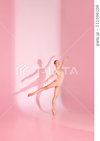 Blushing Balletic. Slim and tender woman, ballerina dancer in pink attire poses against subtle backdrop, her shadow reflecting her grace. Blushing Balletic. Slim and tender woman, ballerina dancer in pink attire poses against subtle backdrop, her shadow reflecting her grace. 111306100