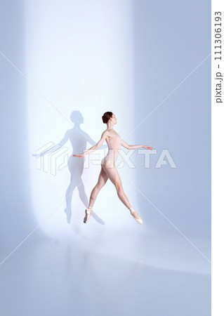 Ballet Beauty. Body-Size Portrait of athlete young woman showcases balletic prowess in pink sport swimsuit and pointe against white backdrop, casting delicate shadow. Ballet Beauty. Body-Size Portrait of athlete young woman showcases balletic prowess in pink sport swimsuit and pointe against white backdrop, casting delicate shadow. 111306193