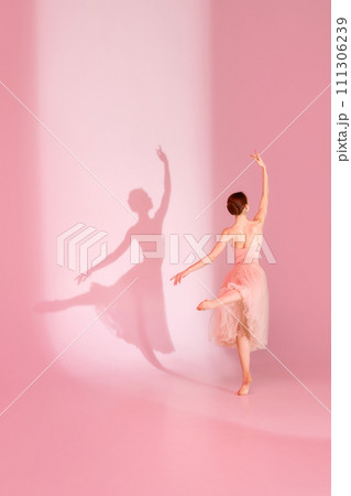 Balletic Beauty. Classic ballerina dances barefoot in pink dress against pastel pink background with her shadow. 111306239