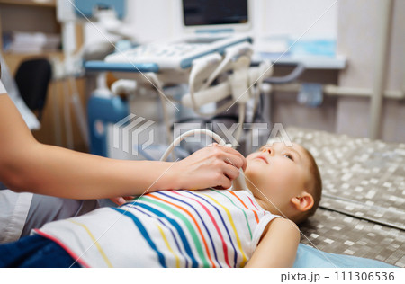Boy undergoing thyroid ultrasound examination. Doctor examining kid throat in clinic with equipment. Boy undergoing thyroid ultrasound examination. Doctor examining kid throat in clinic with equipment. 111306536