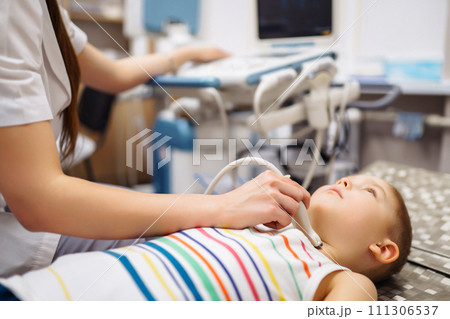 Boy undergoing thyroid ultrasound examination. Doctor examining kid throat in clinic with equipment. Boy undergoing thyroid ultrasound examination. Doctor examining kid throat in clinic with equipment. 111306537