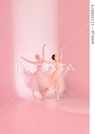 Graceful Ballet. Young woman, classic ballerina dancing barefoot in pink dress against pastel studio background with her shadow. 111306674