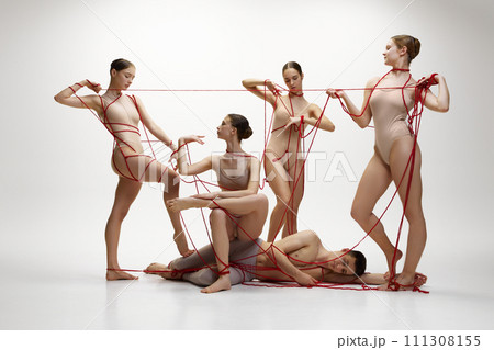 Domination and power of feminism. Ballet art. Man lying of floor while four girls standing near connected with red string against white studio background 111308155