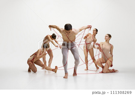 Leaving comfort zone, freedom. Male ballet dancer connected with red strings to ballerinas against white studio background Leaving comfort zone, freedom. Male ballet dancer connected with red strings to ballerinas against white studio background 111308269