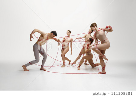 Graceful ballet dancers performing with red string connected to young man against white studio background. Social connections Graceful ballet dancers performing with red string connected to young man against white studio background. Social connections 111308281