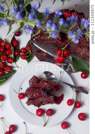 Chocolate cake with sweet cherry, cup of tea and bouquet of blue flowers on white background.. Chocolate cake with sweet cherry, cup of tea and bouquet of blue flowers on white background.. 111309975