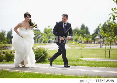 The bride and groom run along the road together The bride and groom run along the road together 111310349