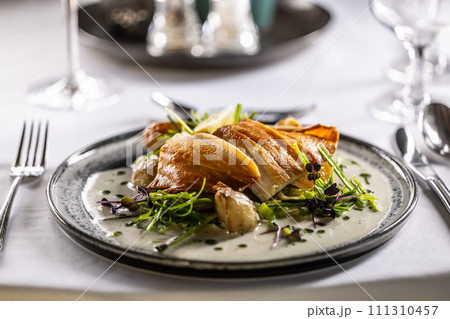 Lightly smoked trout fillet, baked potatoes, beurre blanc sauce, leek and lime dressing. Creatively served fish on a plate in restaurant 111310457