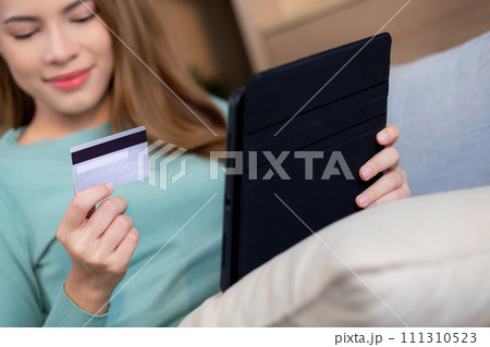 Young asian woman sitting on sofa using digital tablet shopping online with credit card buying. 111310523