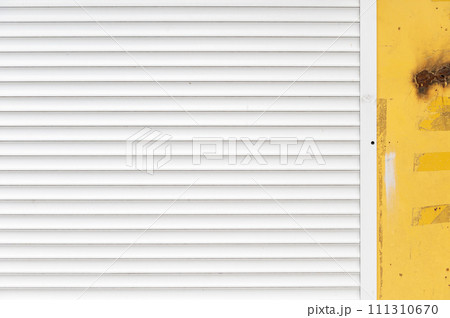 White blinds on the yellow wall of the garage. Yellow textured concrete wall with white blinds background. 111310670