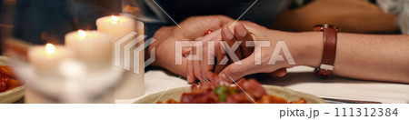 Header of hands of young intercultural valentines sitting by served table with homemade food and burning candles during festive dinner 111312384