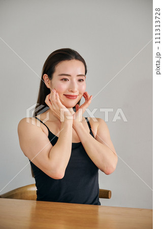 顔をマッサージして肌のお手入れをする30代女性 111313728